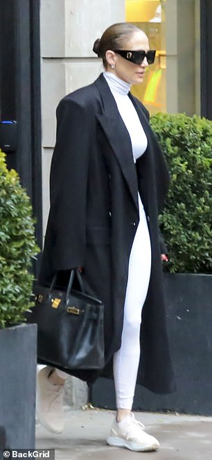 She also wore a white turtleneck crop-top with matching leggings and sneakers beneath a black double-breasted maxi-coat featuring massive shoulder pads