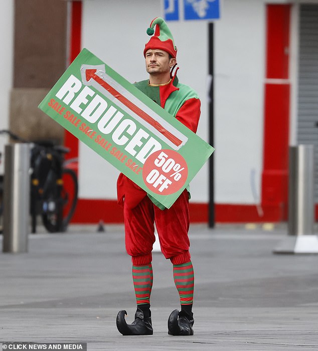 As he got into character and started filming the action movie, Orlando was seen holding up a large 'reduced sale 50% off' sign which had an arrow pointing down the street