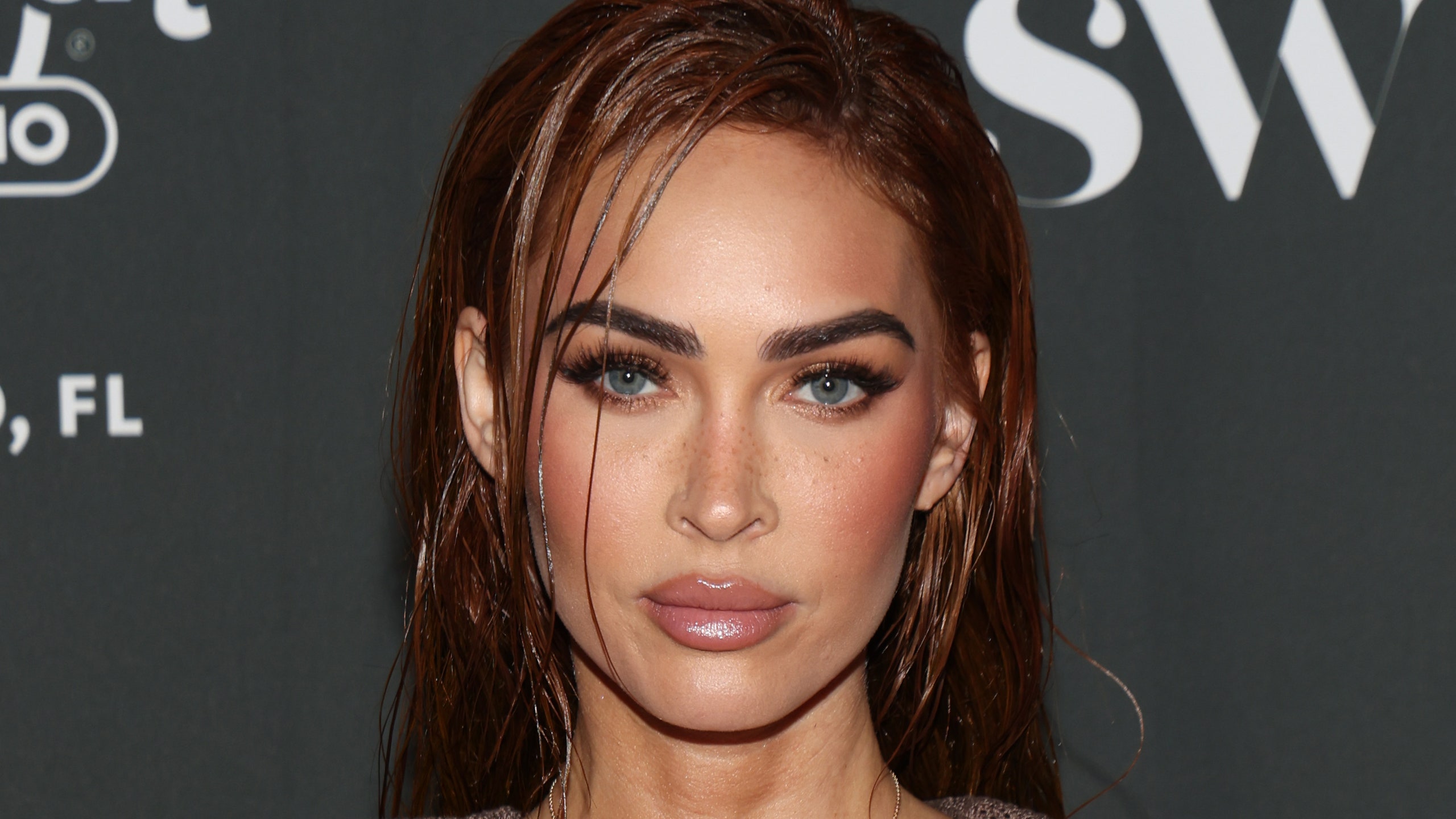 Megan Fox appears at an event in a brown dress. She wears her hair in wet look waves.