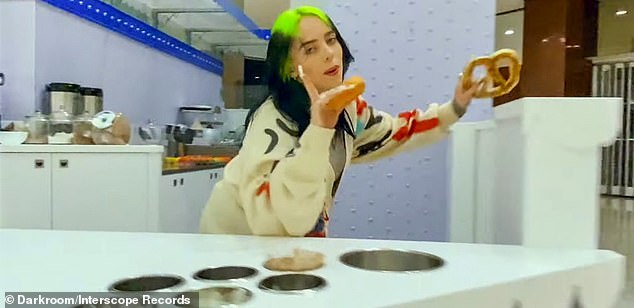 More is more: She croons for the camera while double fisting a donut and pretzel, singing lyrics like 'I'm sorry, I don't think I caught your name'