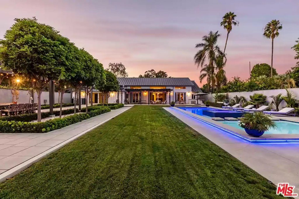 Across a small grass plot, a lit raised pool has stone steps leading past an in-pool jacuzzi to a lounging patio area.