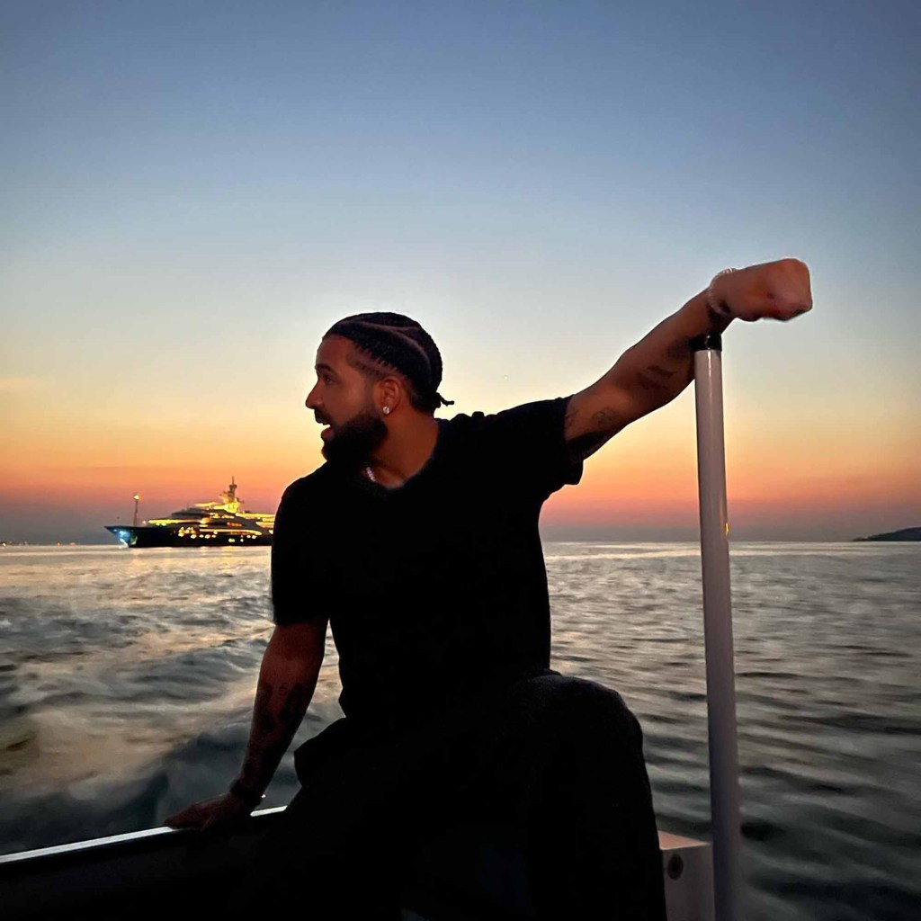 Drake on a boat with the yacht in the background.